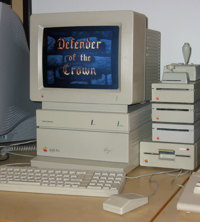 An Apple IIgs computer with floppy drives and a joystick, its monitor showing the title screen of the game Defender of the Crown